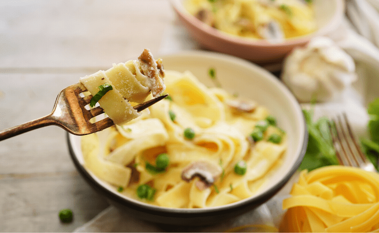 closeup of fork with vegan cannabis infused fettuccine Alfredo wrapped around it in front of bowl of it