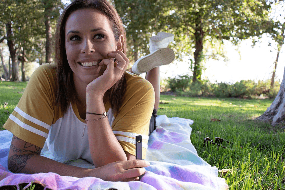 woman vaping outside in the park with purple skin on her vape