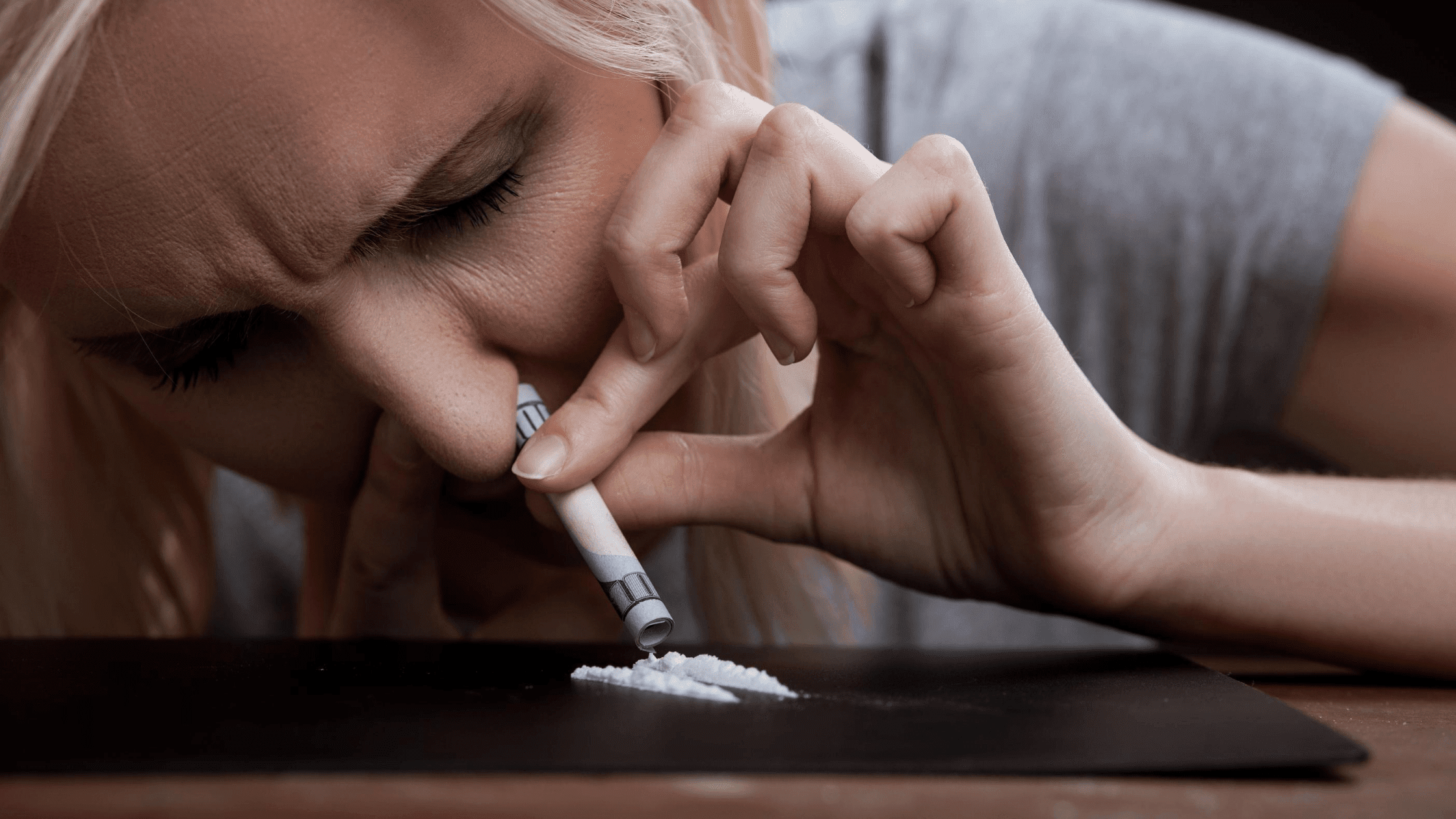 blonde woman abusing cocaine by snorting it up her nose with a rolled up hundred dollar bill