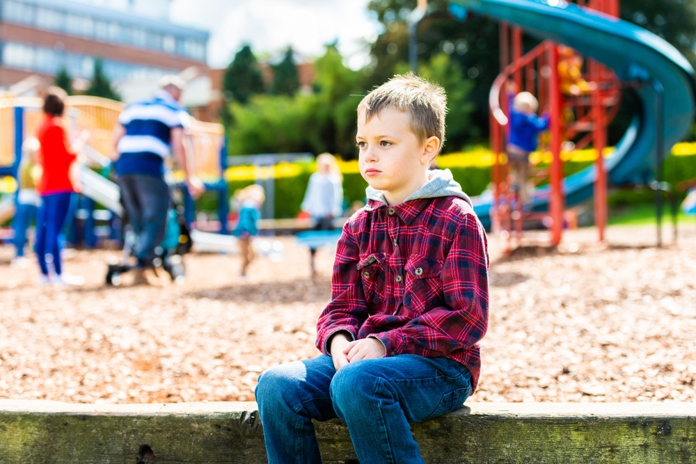 young white boy with ADHD sitting alone at playground