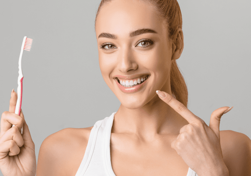 woman brushing teeth pointing at her beautiful smile