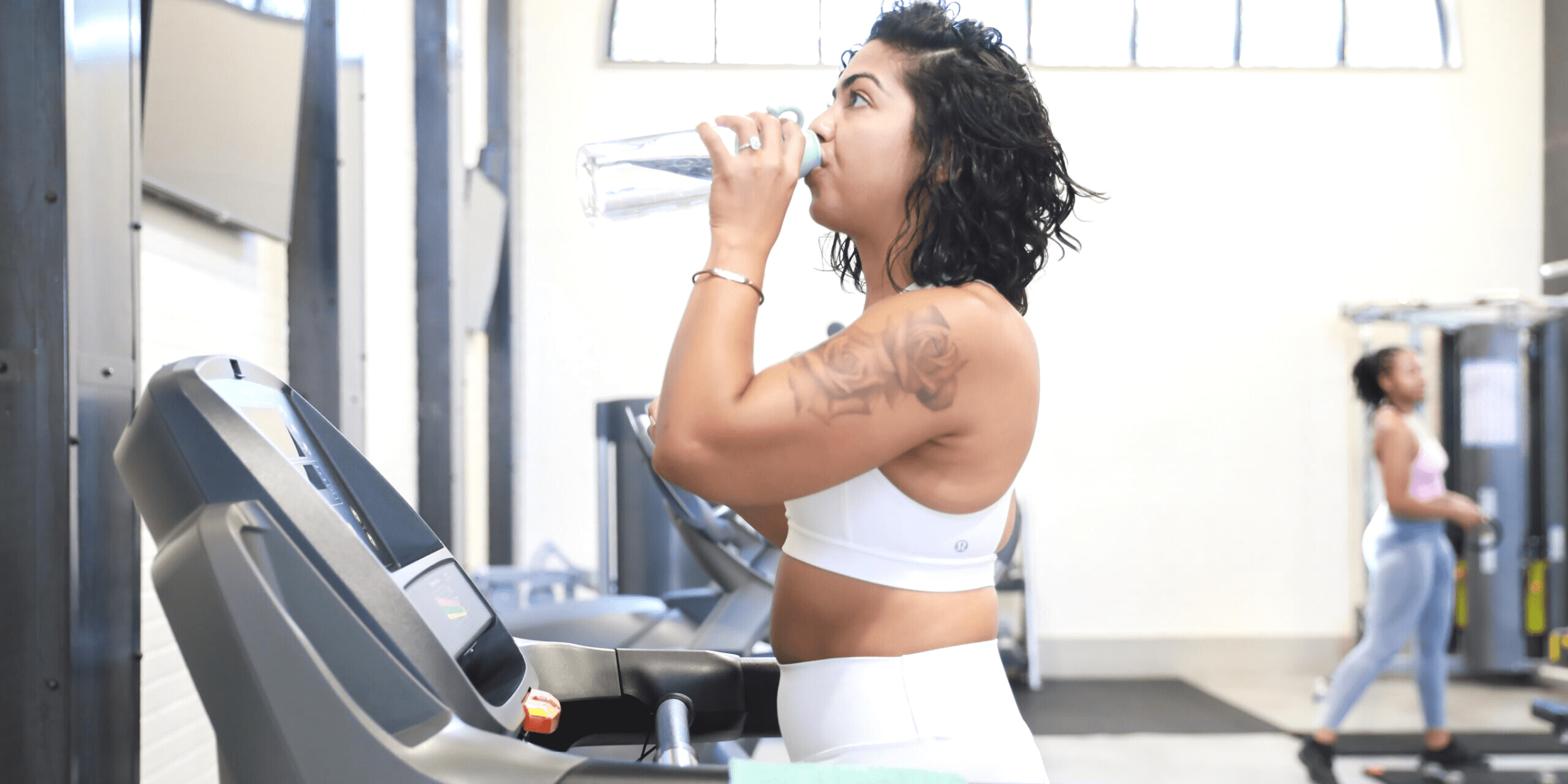 young woman drinking water while working out at the gym