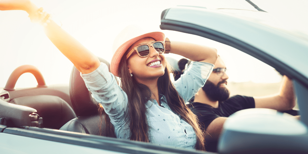 happy young woman with sunglasses in car on road trip with her boyfriend