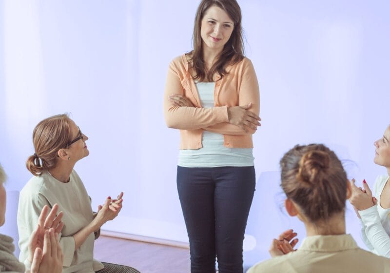 woman at AA meeting successful recovering addict getting praise in group therapy