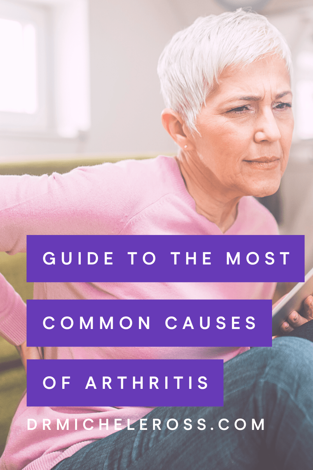 older woman in pink sweater holding back in pain from arthritis