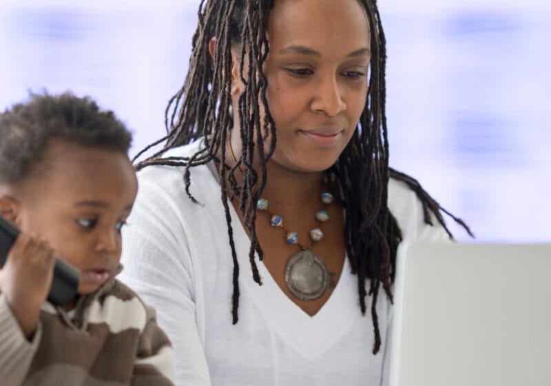 mom working remotely on her laptop from home next to her son holding tv remote control