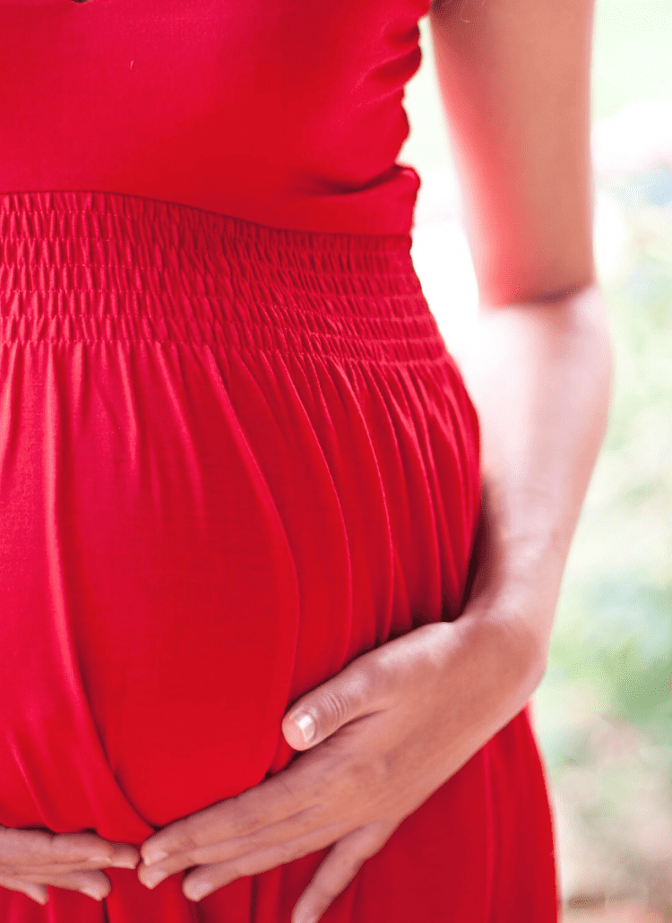 pregnant woman in red dress holding her baby bump