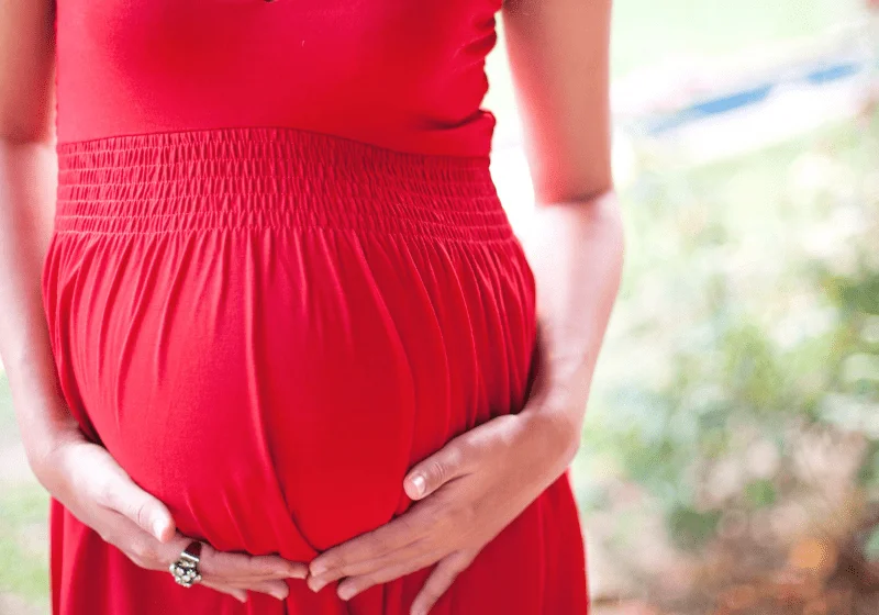 pregnant woman in red dress holding her baby bump