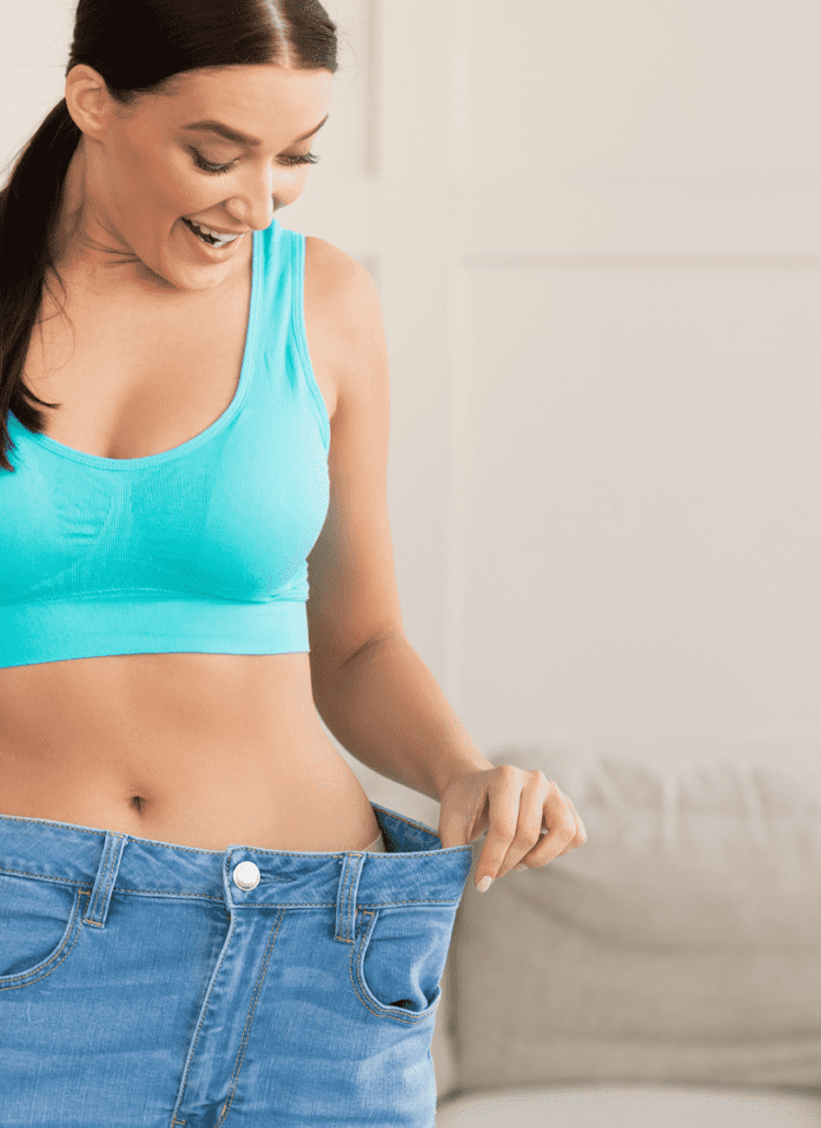 woman in blue sports bra admiring weight loss in jeans