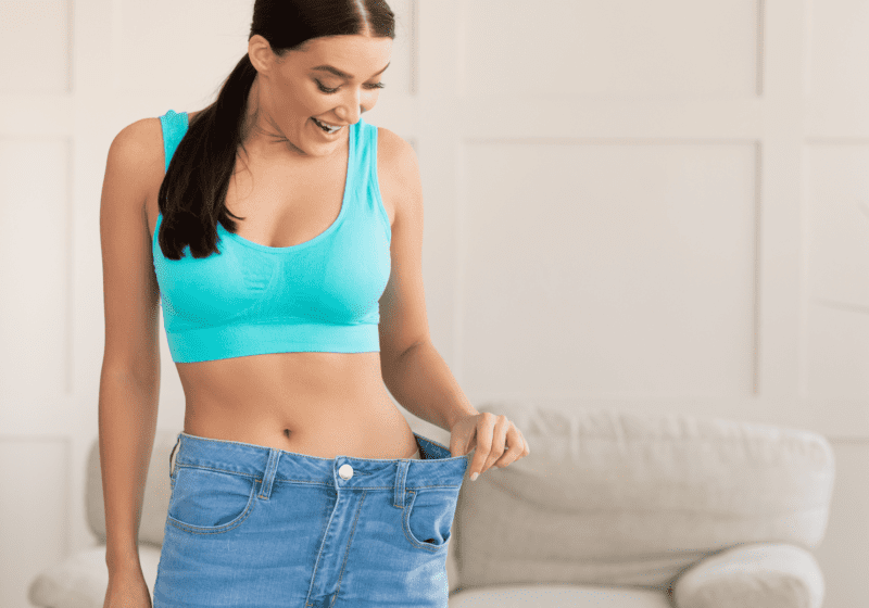 woman in blue sports bra admiring weight loss in jeans