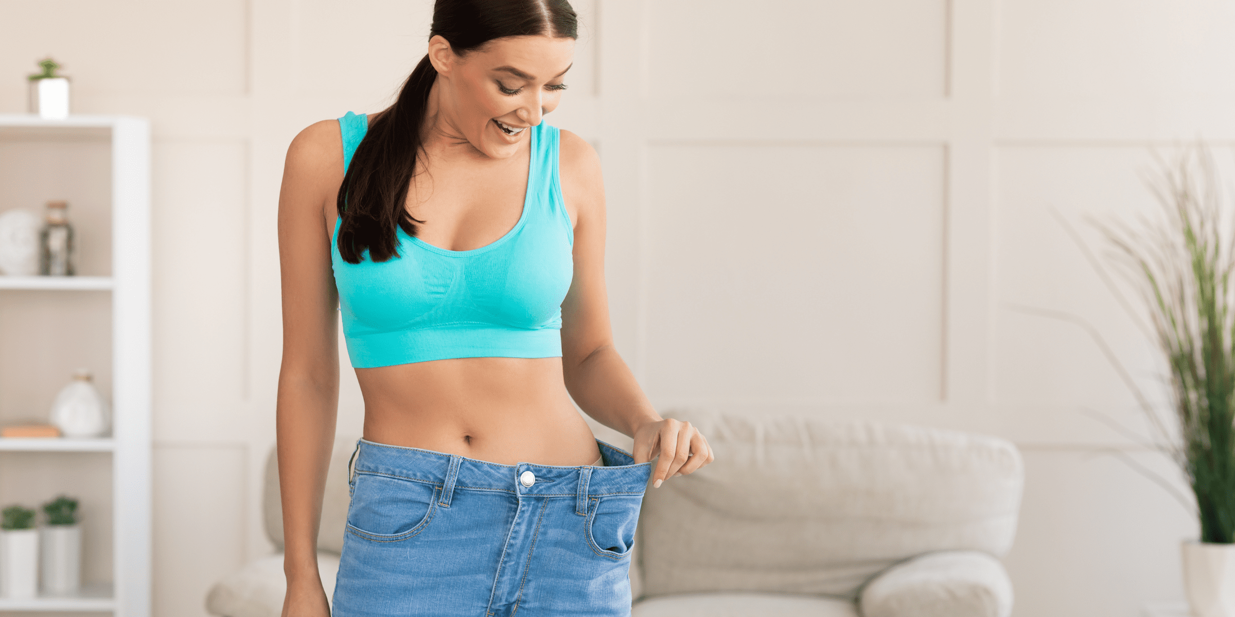 woman in blue sports bra admiring weight loss in jeans