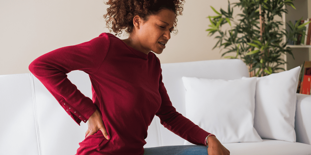 black woman in pain holding back on couch