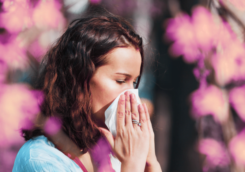 married woman outside with pollen allergies sneezing into tissue