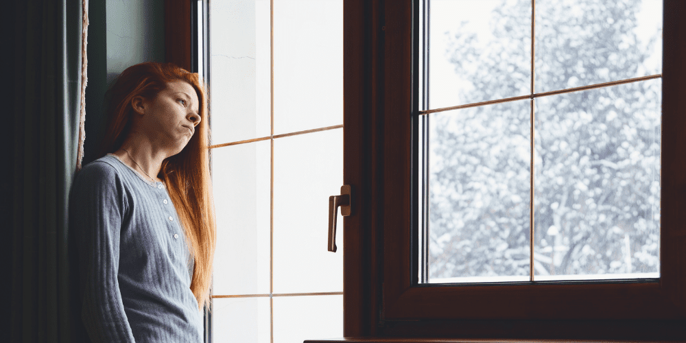 young woman with depression staring out winter window