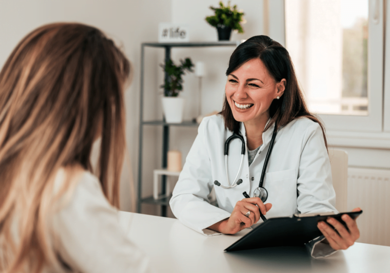 woman doctor smiling talking to satisfied female patient with long hair