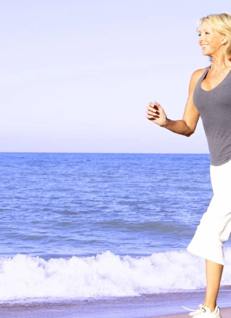 older woman running on the beach to reduce stress