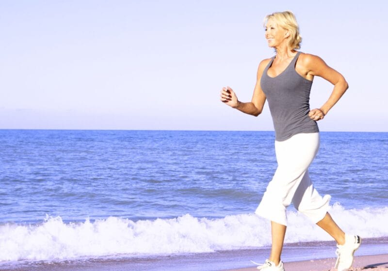 older woman running on the beach to reduce stress