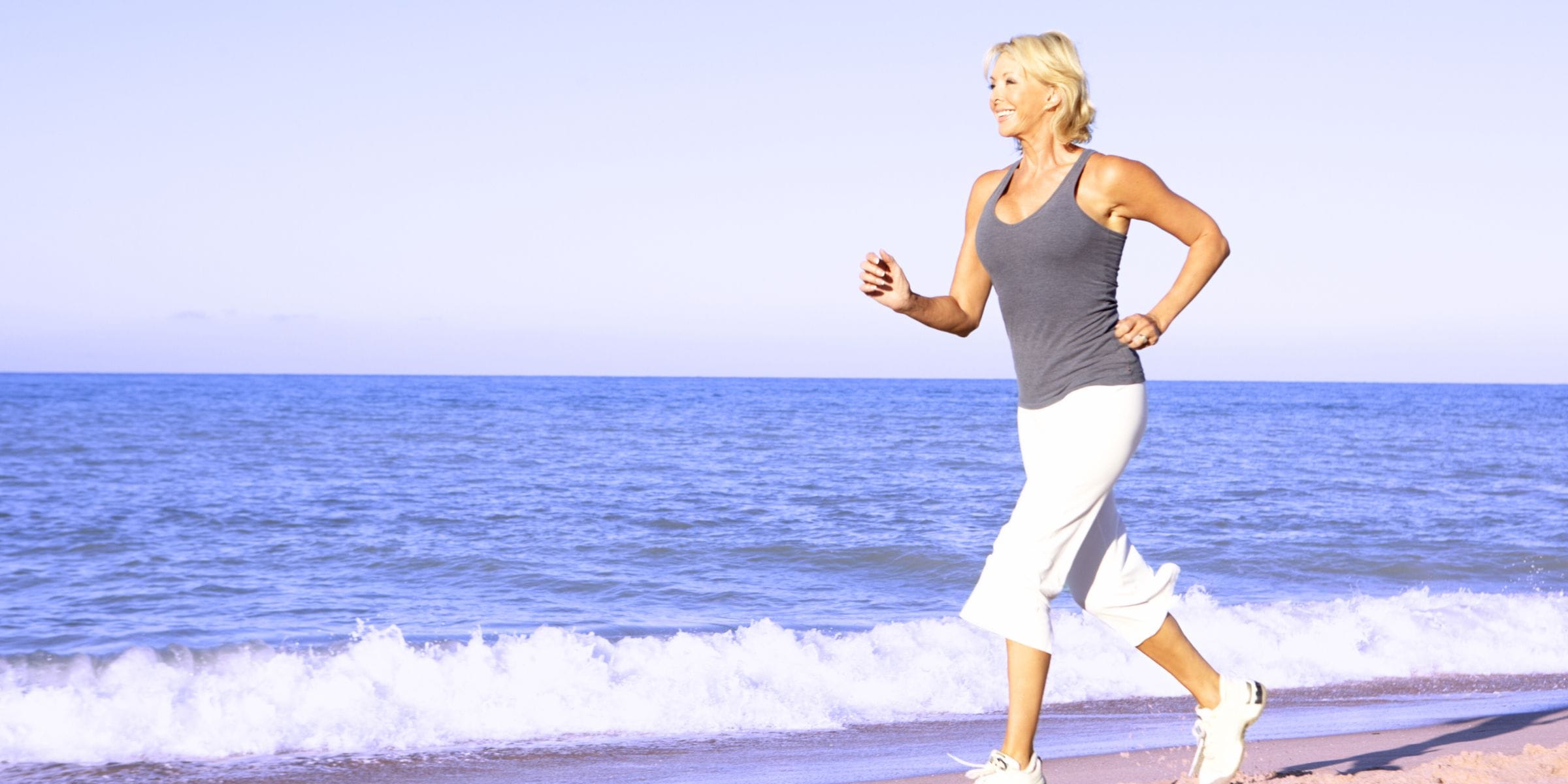 older woman running on the beach to reduce stress