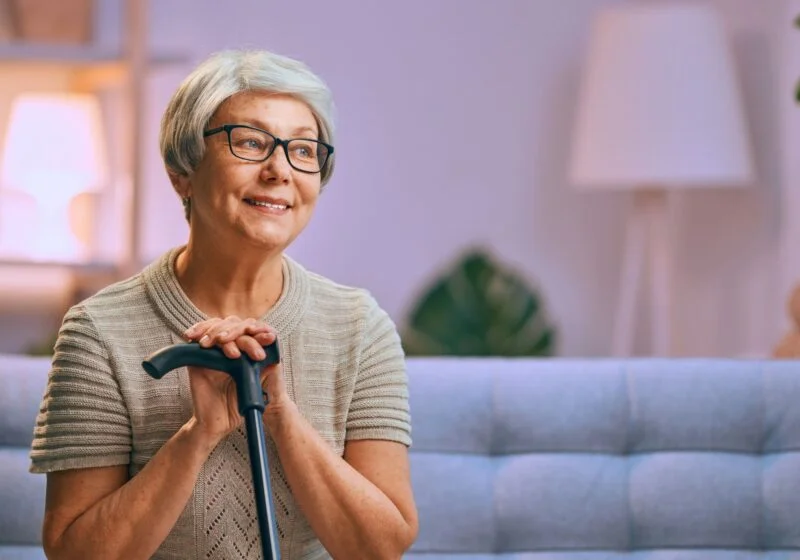 senior woman with arthritis pain resting with cane on couch