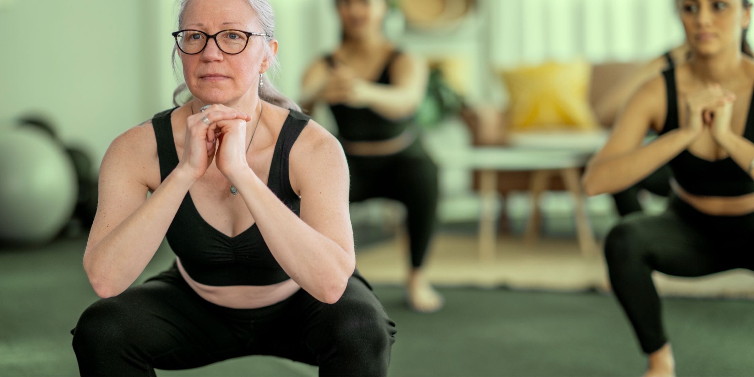 older woman with glasses squatting in an exercise class to get healthy