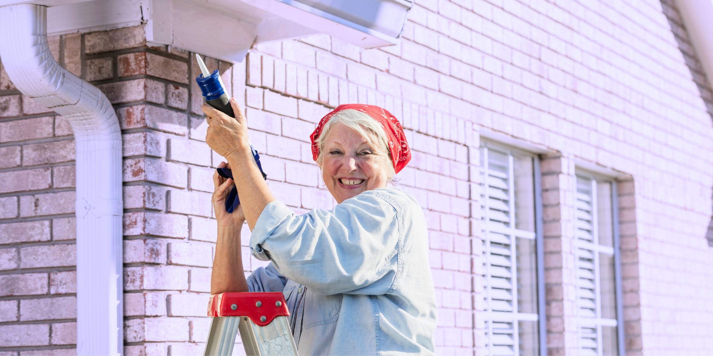 older woman doing home maintenance outside caulking exterior of house