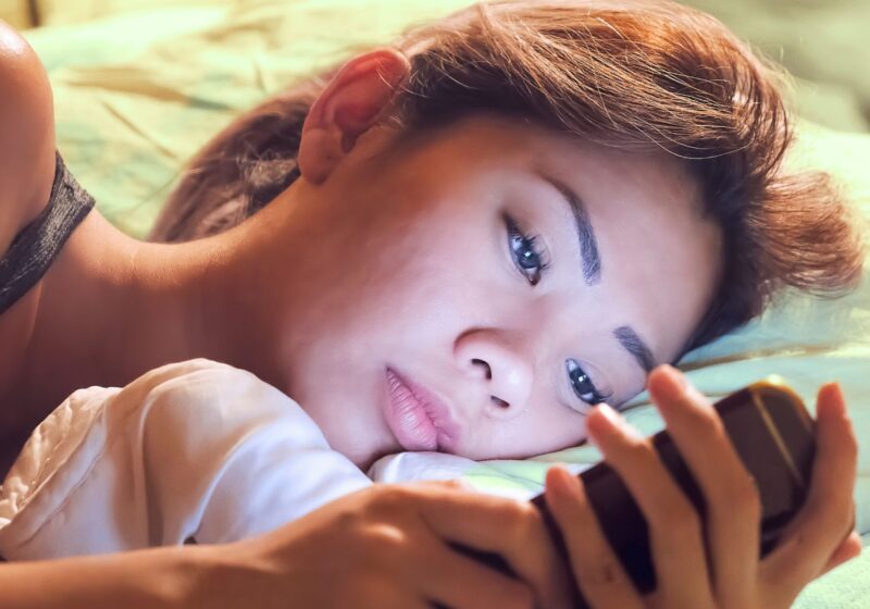 asian woman scrolling on instagram on phone before bed can't sleep and depressed