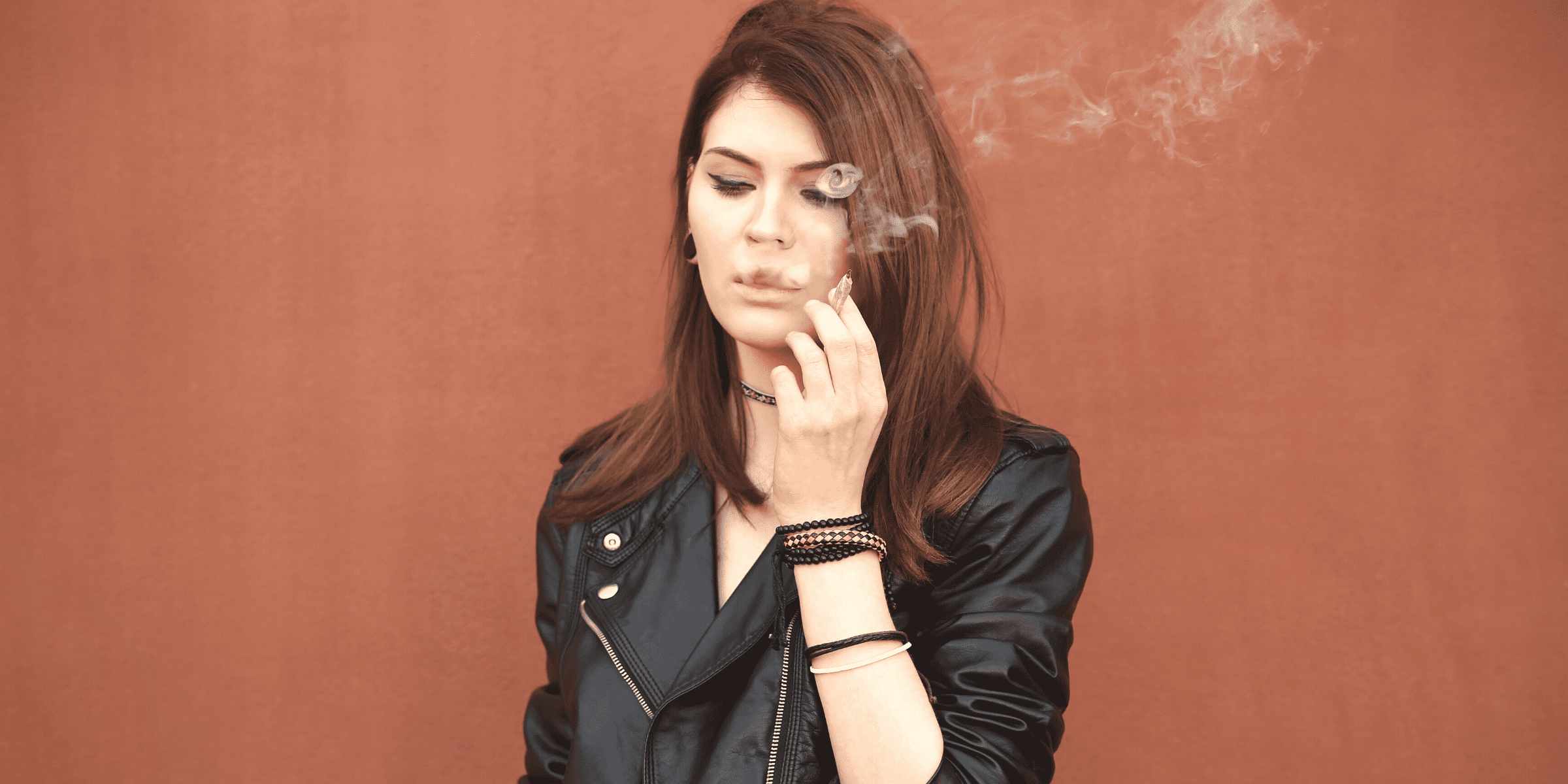 young woman in motorcycle jacket smoking weed via marijuana joint