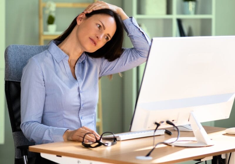 executive woman stretching neck while sitting at an office computer