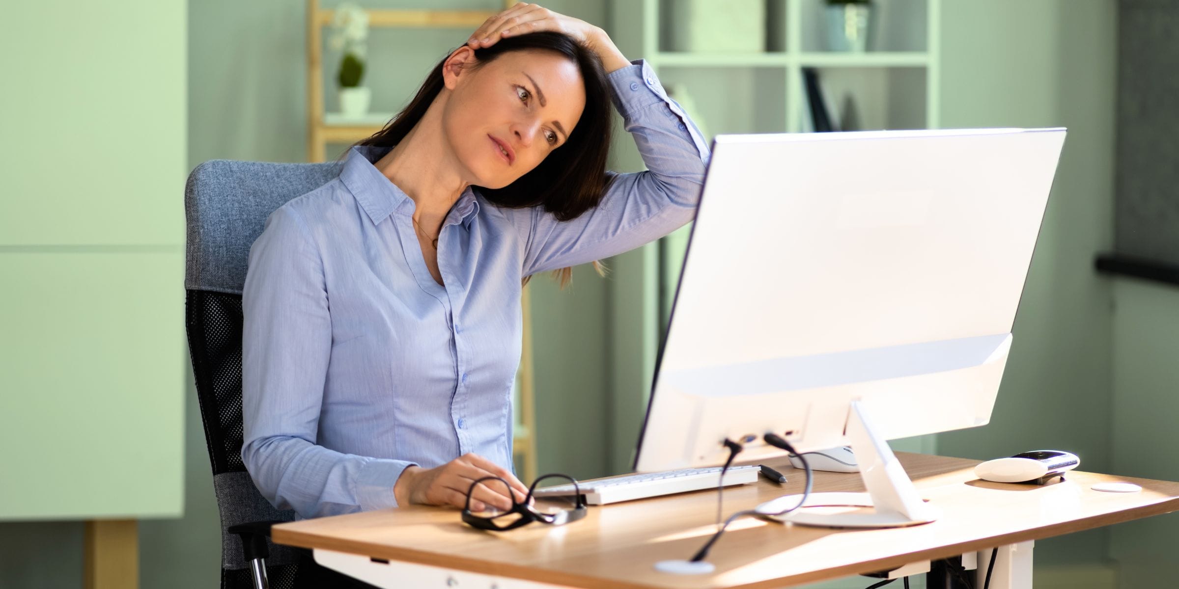 executive woman stretching neck while sitting at an office computer