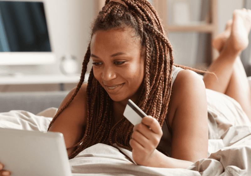 Black woman holding credit card buying medication online in her bed
