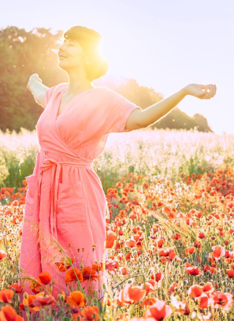 happy woman standing in a field of poppy flowers glowing