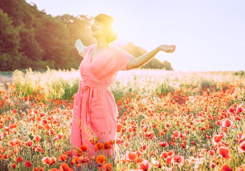 happy woman standing in a field of poppy flowers glowing