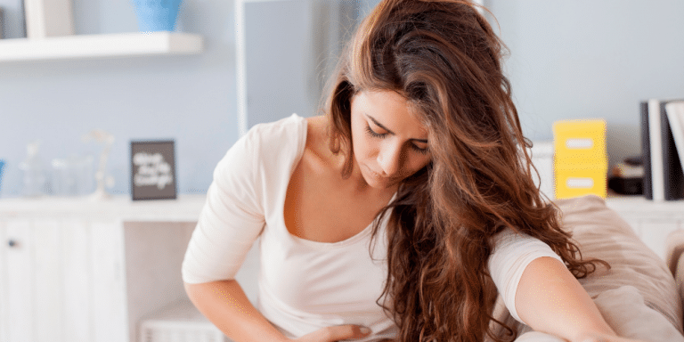 white woman in pain from period cramps looking down at floor