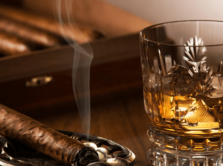 cigar burning next to cigar humidor and glass of whiskey