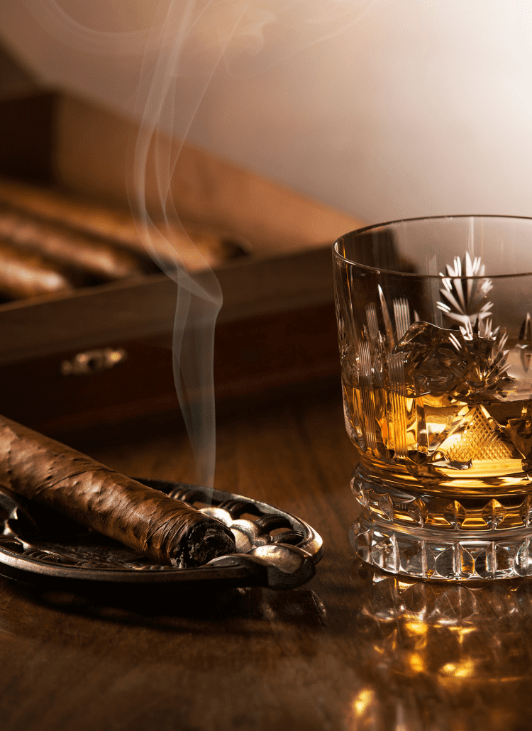 cigar burning next to cigar humidor and glass of whiskey