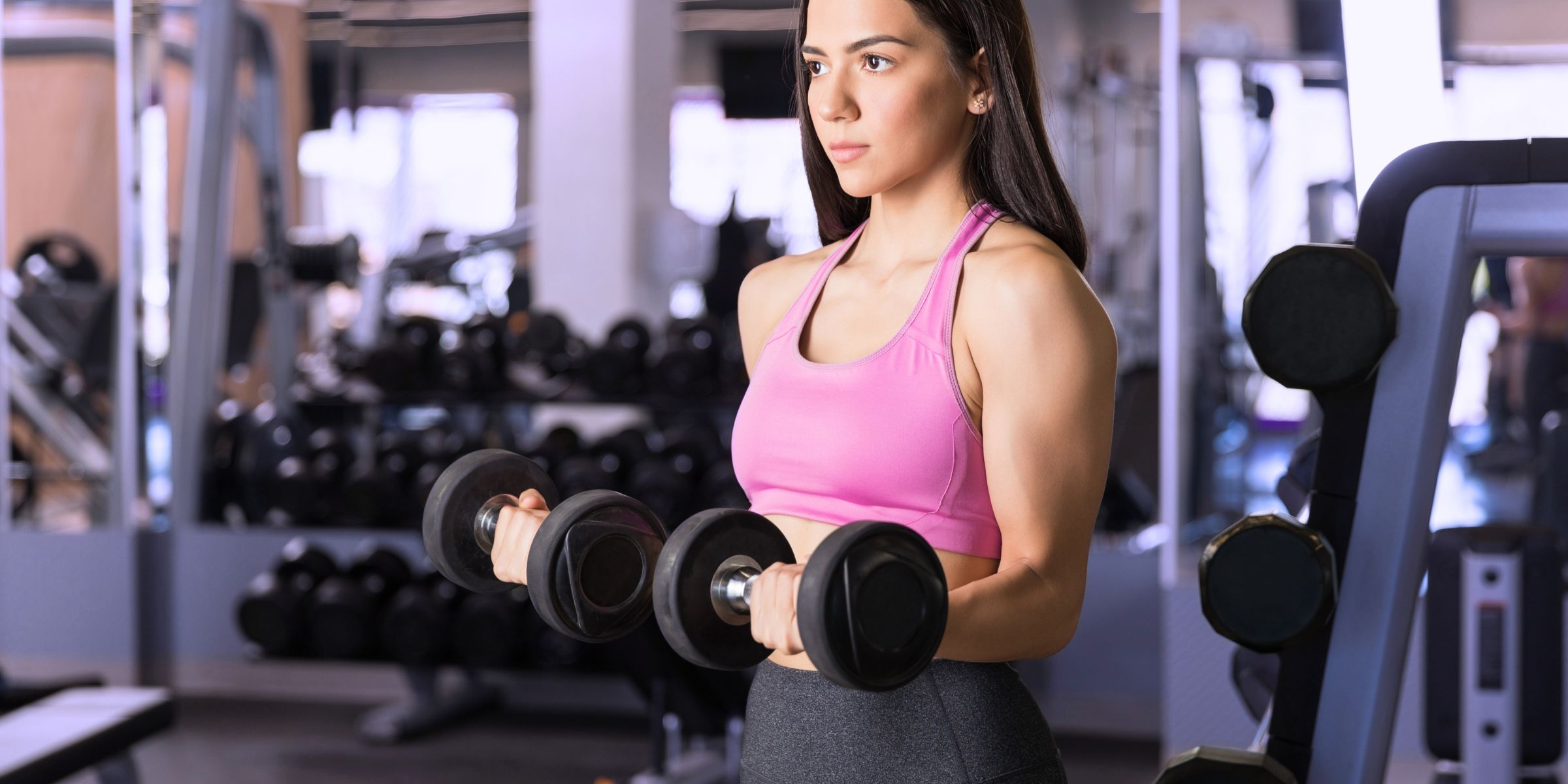 woman in pink sports bra with dumbbells at the gym